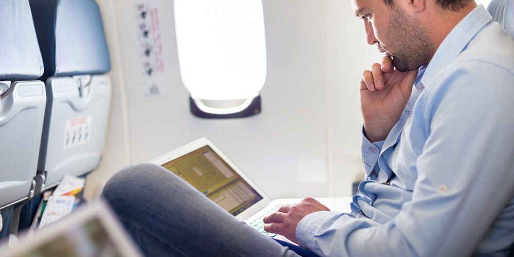 business man on plane with laptop open